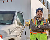 Confident driver standing with arms crossed on truck parking lot and looking at camera.